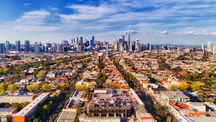 Aerial view of Melbourne, stretching from an outer residential and commercial suburb to the CBD. Daylight and blue skies.